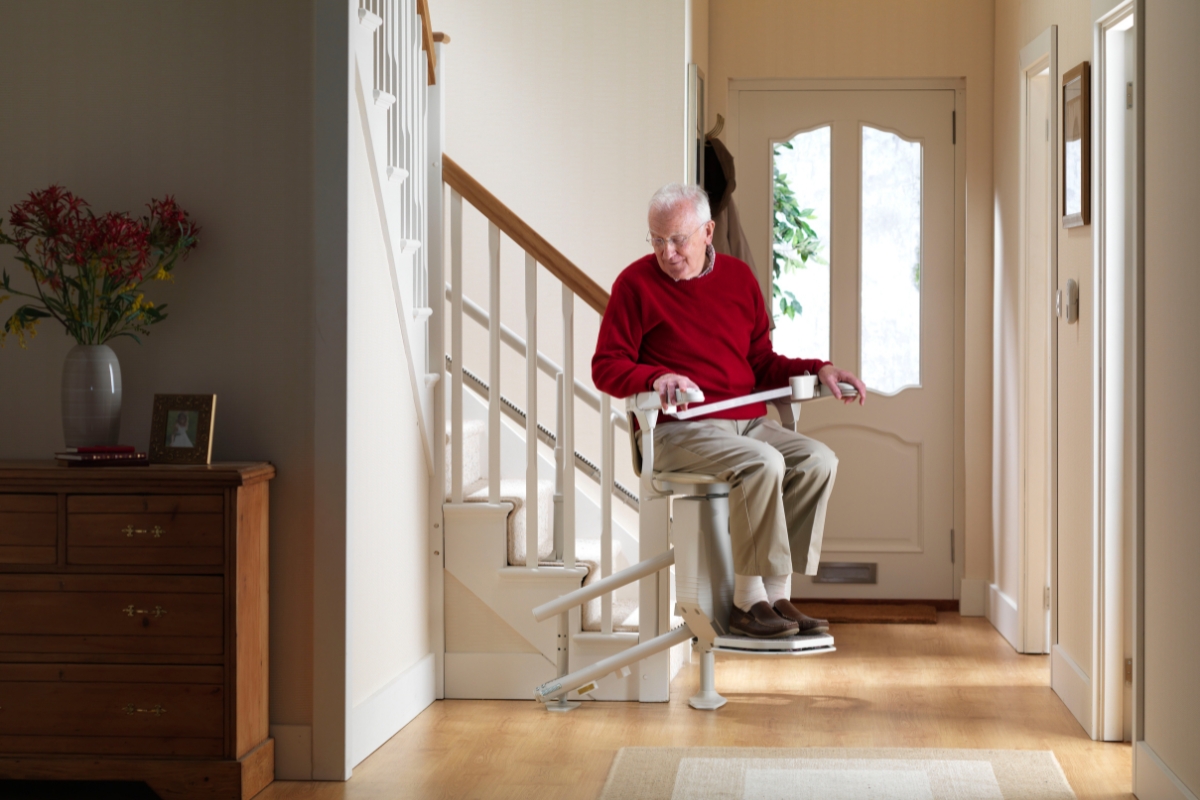 Older man riding a straight stairlift beside the front door in a bright hallway